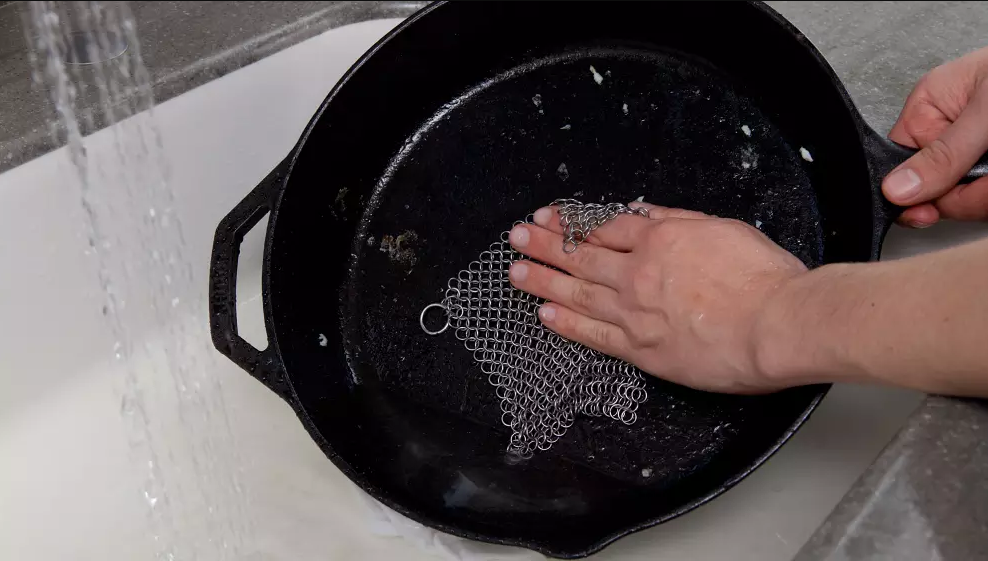 cast iron skillet being cleaned with a chainmail scrubber