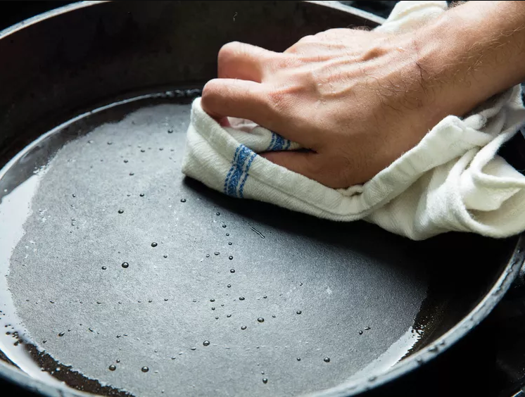 cast iron skillet being dried with a clean dish towel