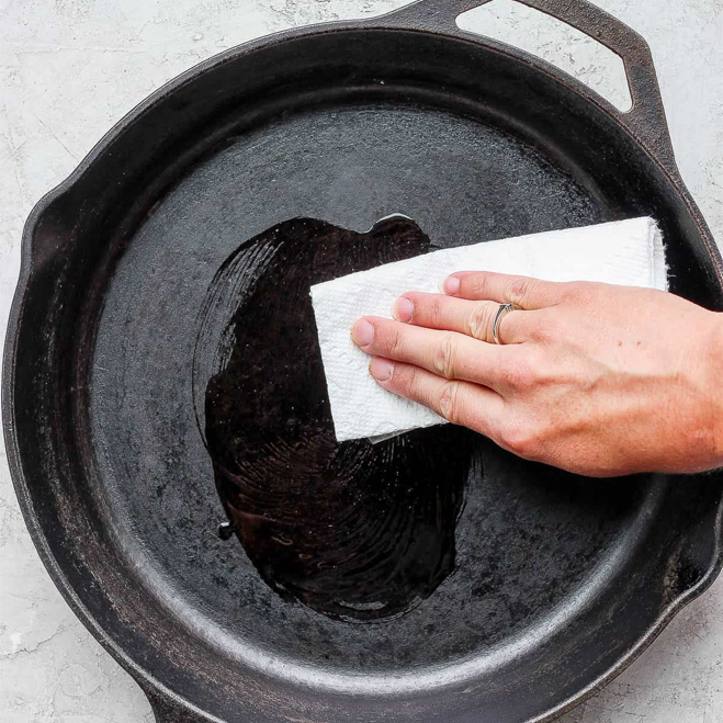 cast iron skillet being seasoned by applying a thin layer if cooking oil